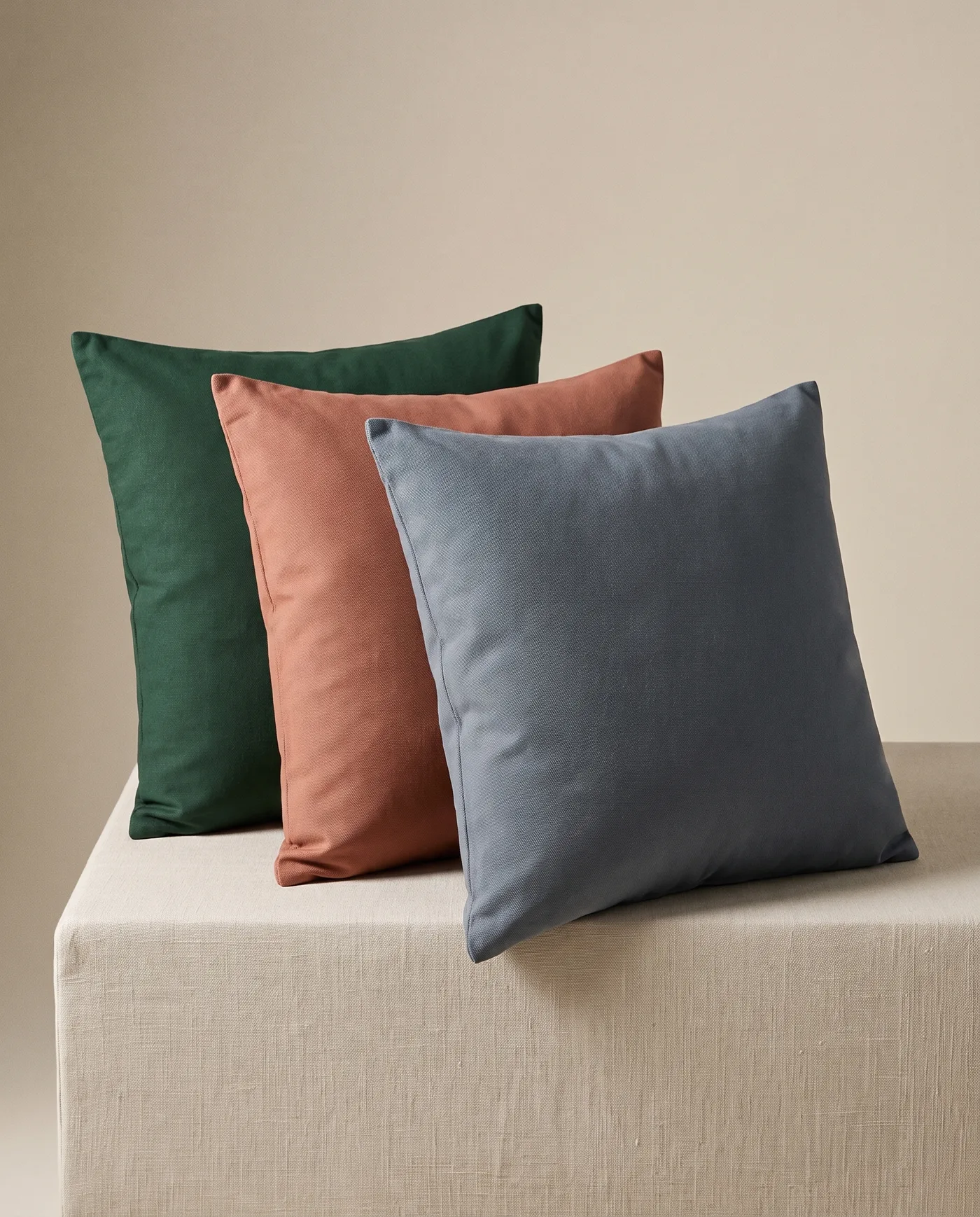 Three cotton cushion covers in forest, clay and slate leaning together on a linen plinth.