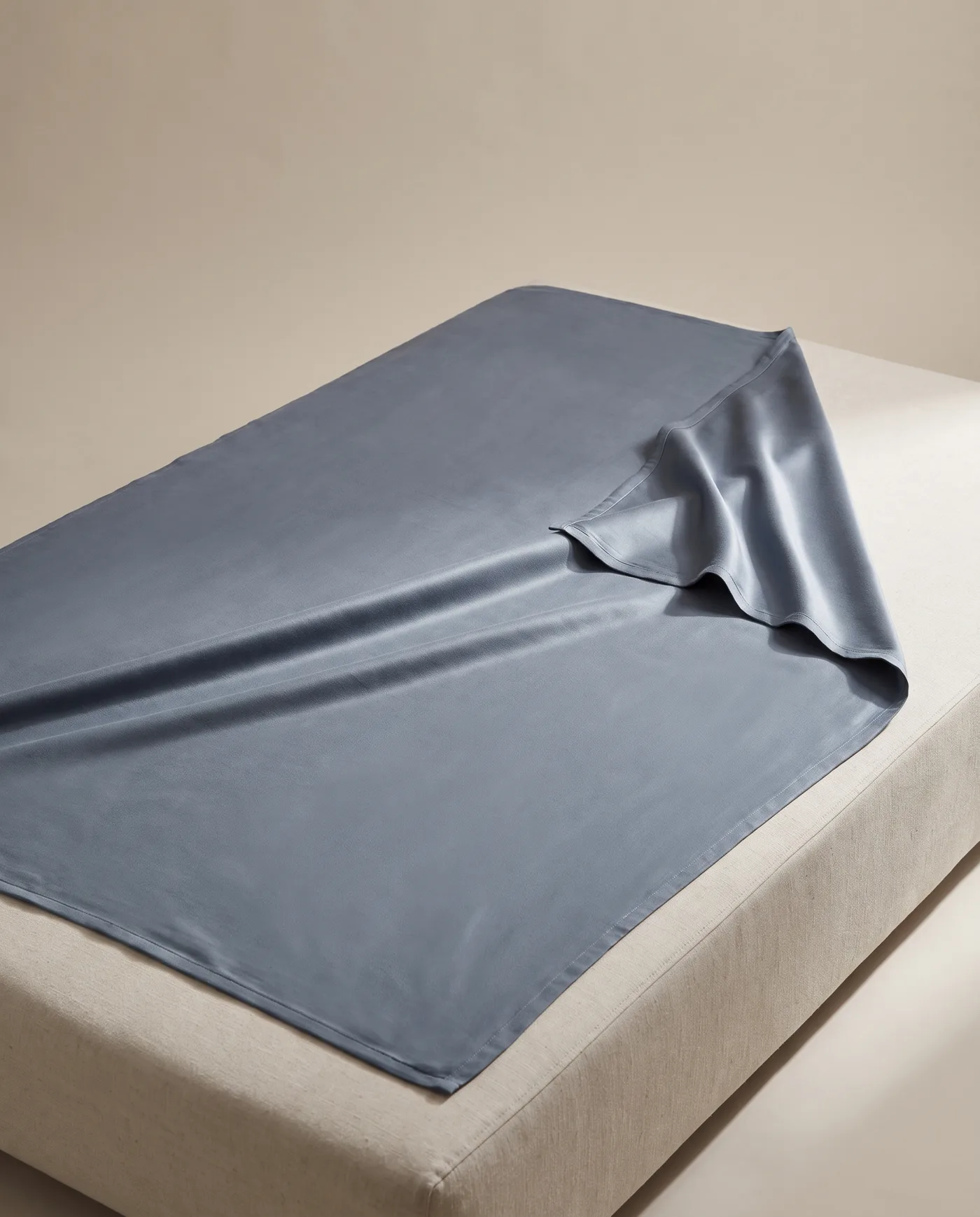 A slate blue bamboo blanket laid flat with one corner turned back, on a linen plinth.