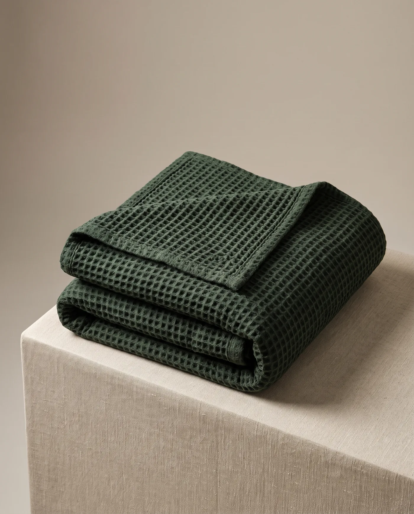 A deep forest green waffle-weave cotton throw folded in thirds on a linen plinth.